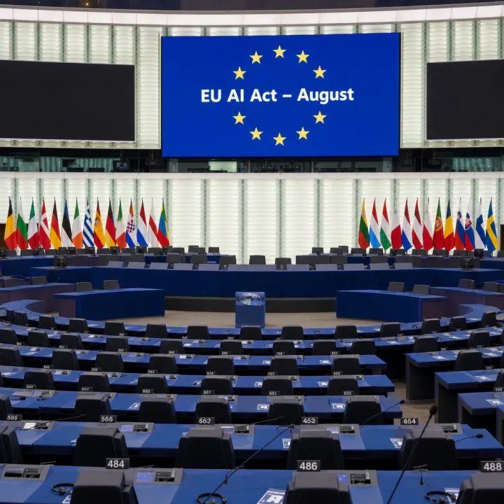 Fotorealistische Darstellung: Eine EU-Kommissarin hält vor einer Europaflagge ein Dokument mit der Aufschrift „EU AI Act – August" in die Höhe, davor Journalisten mit Mikrofonen.