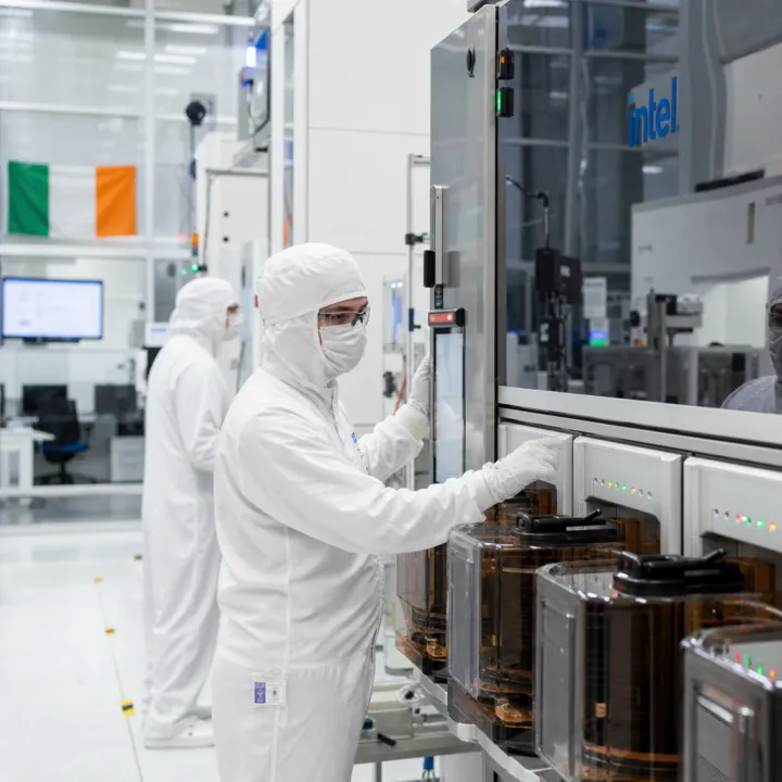 Technicians in cleanroom suits at a wafer fabrication tool bearing the Intel logo.
